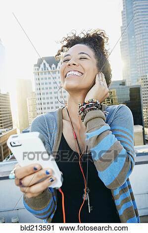Stock Image - Mixed race woman listening to earbuds on urban rooftop. Fotosearch