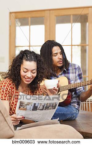 Stock Image - Mixed race woman listening to husband play guitar. Fotosearch