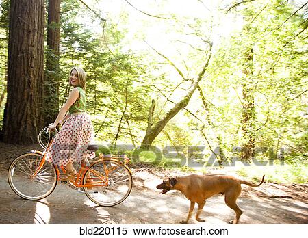 Stock Photography - Mixed race woman riding bicycle with dog. Fotosearch