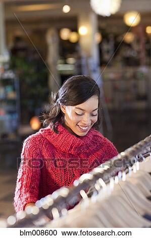 Stock Image - Mixed race woman shopping for clothing in store. Fotosearch