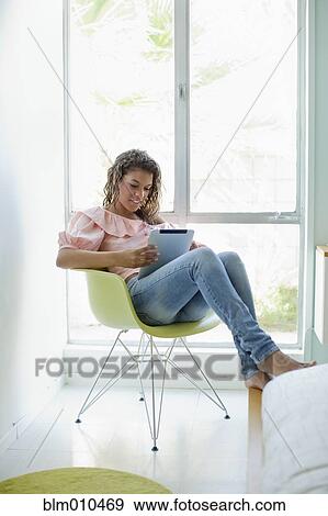 Stock Photo - Mixed race woman sitting in chair using digital tablet. Fotosearch
