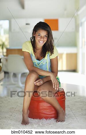 Mixed race woman sitting on ottoman in living room View Large Photo Image Stock Image - Mixed race woman sitting on ottoman in living room. Fotosearch