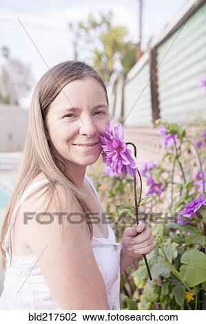 Stock Image - Mixed race woman smelling flowers in garden. Fotosearch
