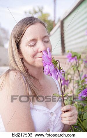 Stock Image - Mixed race woman smelling flowers in garden. Fotosearch