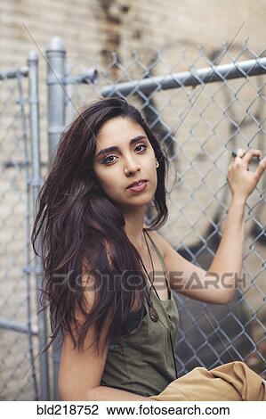 Stock Image - Mixed race woman standing at chain link fence. Fotosearch