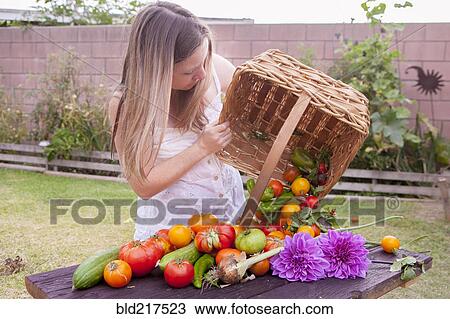 Stock Image - Mixed race woman with basket of vegetables and flowers. Fotosearch