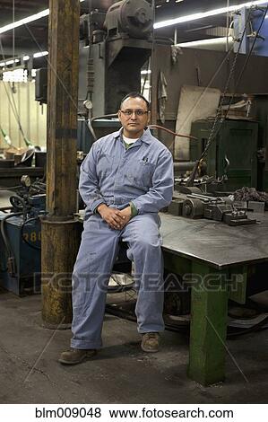 Mixed race worker sitting on table in factory View Large Photo Image Stock Photo - Mixed race worker sitting on table in factory. Fotosearch