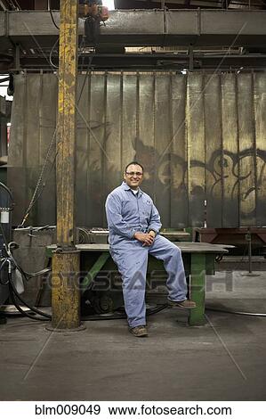 Stock Photo - Mixed race worker sitting on table in factory. Fotosearch