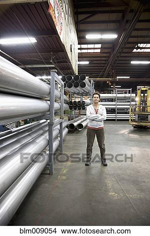 Picture - Mixed race worker standing near metal pipes in factory. Fotosearch