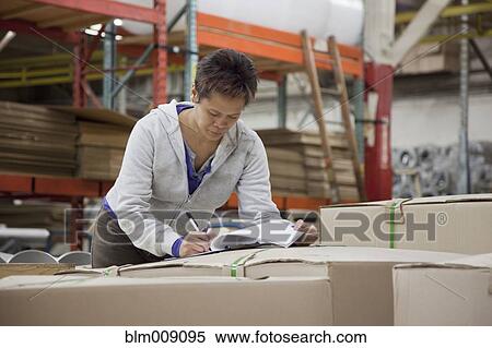 Stock Photography - Mixed race worker writing on clipboard in factory. Fotosearch