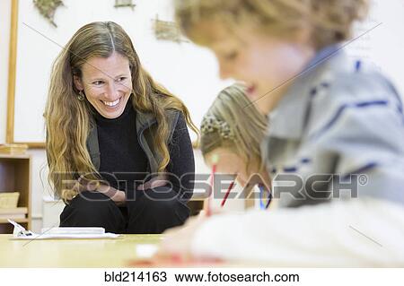 Stock Image - Montessori teacher helping students in classroom. Fotosearch