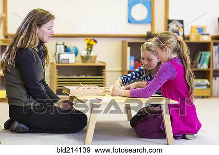 Stock Photo - Montessori teacher helping students in classroom. Fotosearch