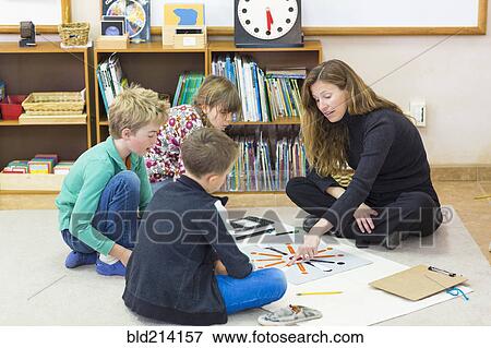 Stock Photo - Montessori teacher helping students in classroom. Fotosearch