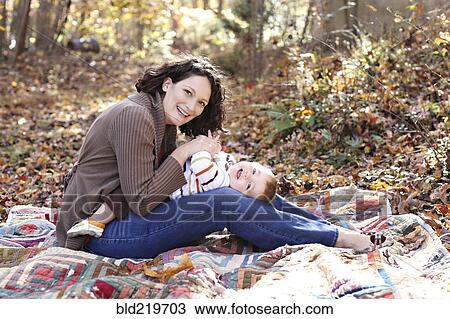 Stock Image - Mother and baby daughter playing on blanket in forest. Fotosearch