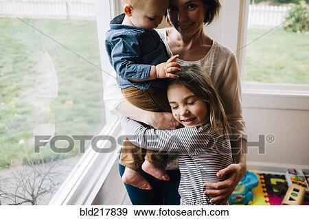 Mother and children hugging at window View Large Photo Image Stock Photo - Mother and children hugging at window. Fotosearch