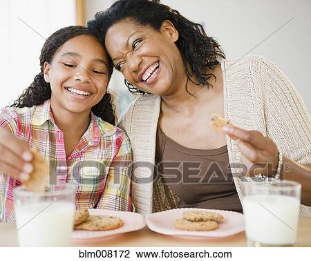 Stock Image - Mother and daughter eating cookies and milk together. Fotosearch