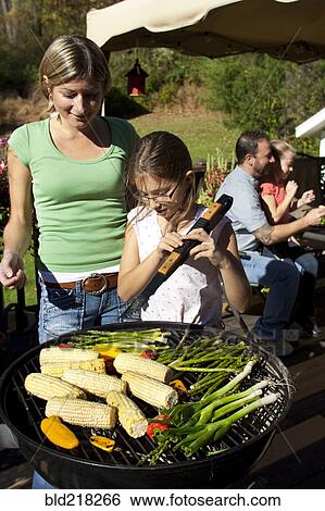 Stock Photograph - Mother and daughter grilling vegetables on patio. Fotosearch