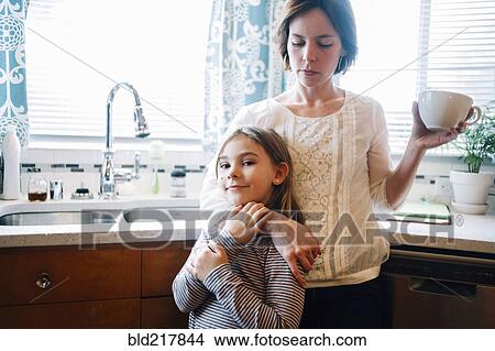 Picture - Mother and daughter hugging in kitchen. Fotosearch