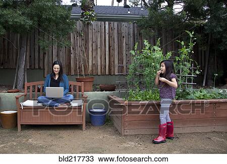 Stock Image - Mother and daughter relaxing in backyard. Fotosearch