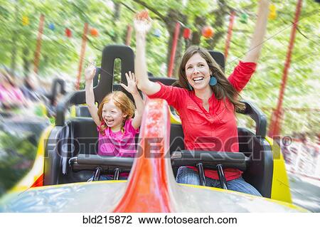 Stock Image - Mother and daughter riding roller coaster in amusement park. Fotosearch