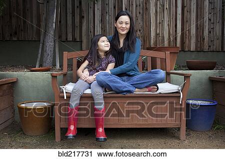 Mother and daughter sitting on bench in backyard View Large Photo Image Stock Image - Mother and daughter sitting on bench in backyard. Fotosearch