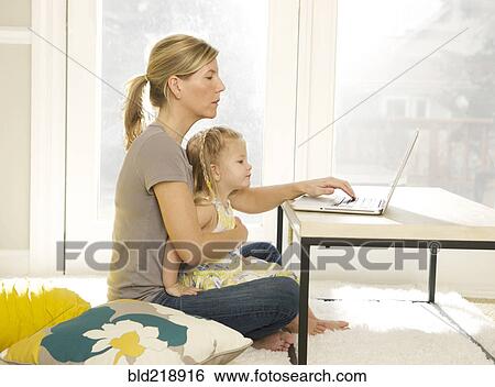 Stock Photograph - Mother and daughter using laptop in living room. Fotosearch