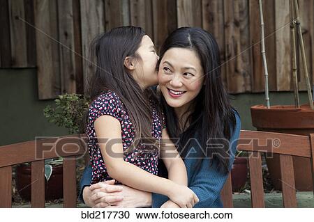 Stock Image - Mother and daughter whispering secrets in backyard. Fotosearch