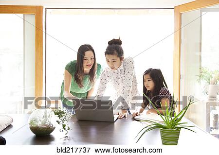 Stock Photo - Mother and daughters using laptop in dining room. Fotosearch