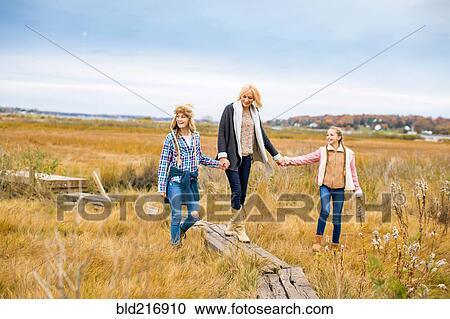 Stock Image - Mother and daughters walking in rural field. Fotosearch