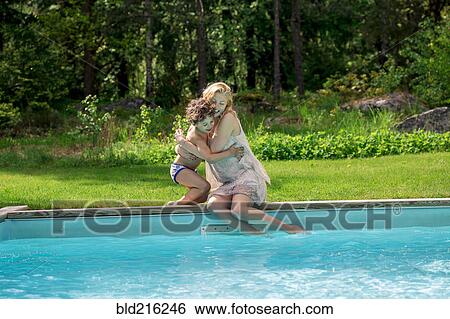 Stock Photograph - Mother hugging son at swimming pool in backyard. Fotosearch