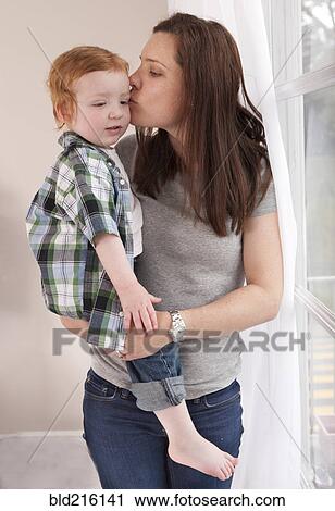 Stock Image - Mother kissing son near window. Fotosearch