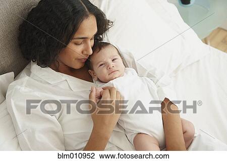 Stock Image - Mother laying in bed holding baby girl. Fotosearch