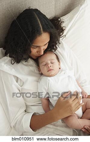 Stock Image - Mother laying in bed holding sleeping baby girl. Fotosearch