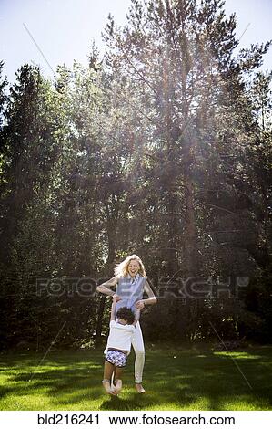 Stock Image - Mother playing with son near trees. Fotosearch