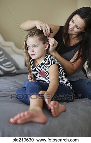 Mother styling hair of daughter on bed View Large Photo Image Stock Image - Mother styling hair of daughter on bed. Fotosearch