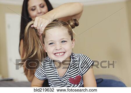 Mother styling hair of daughter on bed View Large Photo Image Stock Image - Mother styling hair of daughter on bed. Fotosearch