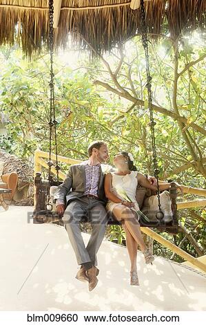 Stock Image - Newlywed couple sitting on swing together. Fotosearch