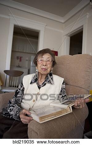 Stock Photography - Older Asian woman looking at photo album. Fotosearch