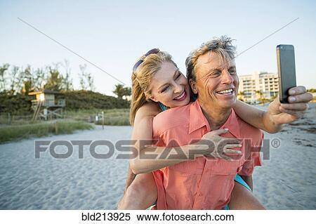 Stock Photography - Older Caucasian couple taking cell phone selfie on beach. Fotosearch