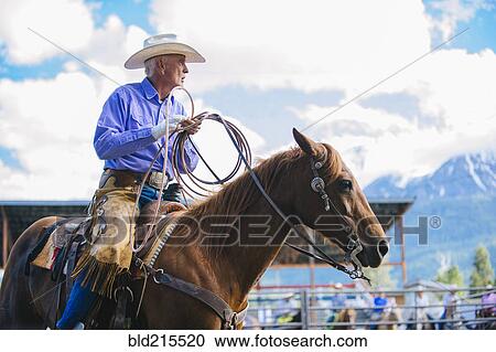 Stock Image - Older Caucasian cowboy riding horse at rodeo. Fotosearch