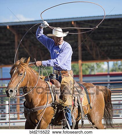 Stock Image - Older Caucasian cowboy throwing lasso at rodeo. Fotosearch