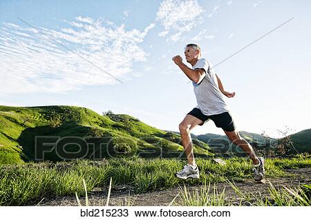 Stock Image - Older Caucasian man jogging on dirt path. Fotosearch
