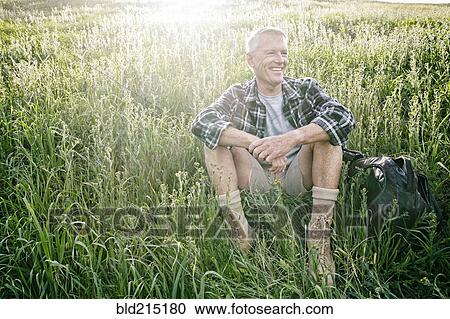 Stock Image - Older Caucasian man sitting on grassy hillside. Fotosearch