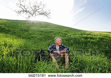 Stock Image - Older Caucasian man sitting on grassy hillside. Fotosearch