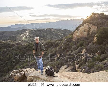 Stock Image - Older Caucasian man standing on rocky hilltop. Fotosearch