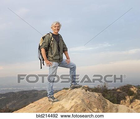 Stock Image - Older Caucasian man standing on rocky hilltop. Fotosearch