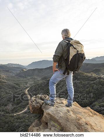 Stock Photograph - Older Caucasian man standing on rocky hilltop. Fotosearch