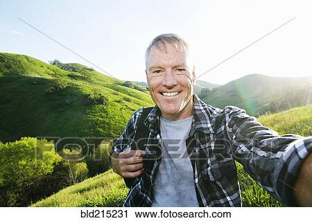 Stock Image - Older Caucasian man taking selfie on rural hilltop. Fotosearch