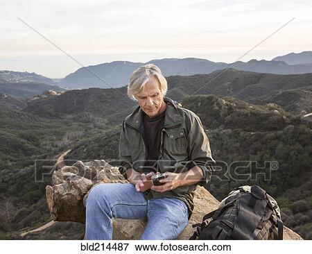 Stock Photo - Older Caucasian man using cell phone on rocky hilltop. Fotosearch