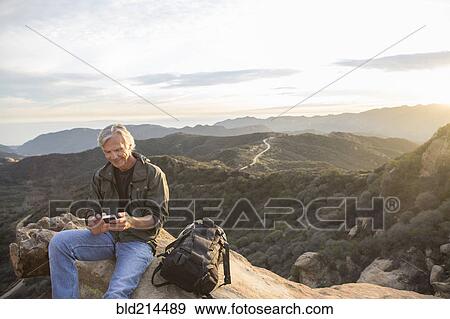Stock Photo - Older Caucasian man using cell phone on rocky hilltop. Fotosearch